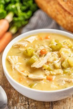 a white bowl filled with chicken and vegetable soup next to bread on a wooden table