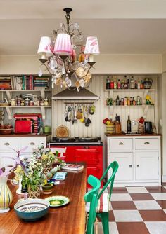 a dining room table with green chairs next to a red stove top oven and cabinets