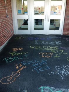 chalk writing on the ground in front of a building with two doors and glass windows