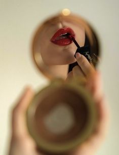 a woman holding a magnifying glass looking at her red lips in the mirror