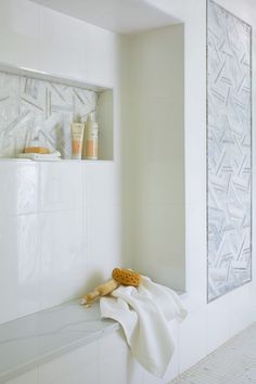 a bathroom with white tiles and towels on the shelf above the bathtub is an open shelving unit