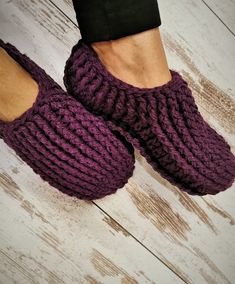 someone wearing purple knitted slippers on top of a wooden floor