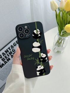 a person holding up a phone case with pandas on it and flowers in the background