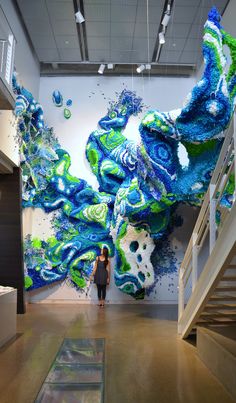 a woman standing in front of a large painting on the side of a wall next to stairs