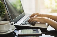 a person typing on a laptop computer at a table with a cup of coffee and cell phone