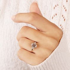 a woman's hand with a diamond ring on her left finger, wearing a white sweater