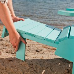 a person reaching for a blue bench on the beach