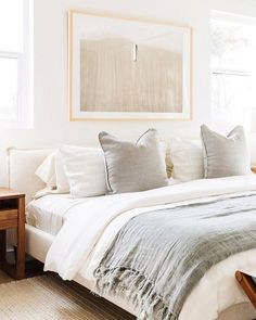 a bed with white linens and pillows in a bedroom next to a painting on the wall