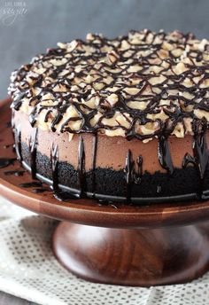 a chocolate cake with nuts on top sitting on a wooden platter, ready to be eaten