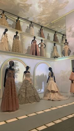 a room filled with lots of mannequins and dresses on display in front of a painting