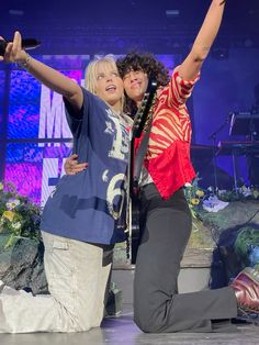 two people on stage with one holding up her arms