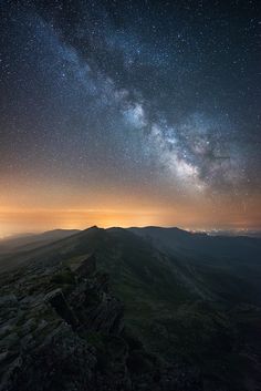 the night sky is filled with stars and clouds above a rocky mountain range in the foreground