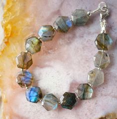 Add a little magic to your everyday look with this beautiful Hexagonal Labradorite Bracelet! Labradorite is a naturally gray stone that flashes shades of blue and green. It is believed to support us through everyday life changes, helping us stay balanced and connected. While the hexagonal shape symbolizes balance and positivity. Together, these two make the perfect pair! When making your bracelet, each stone will be hand-selected for its unique shine and iridescent glow. Tiny gold or silver bead Gift Labradorite Jewelry With Polished Beads, Spiritual Gray Bracelet Jewelry, Faceted Labradorite Bracelets As Gift, Adjustable Labradorite Gemstone Beads Bracelets, Elegant Adjustable Labradorite Beaded Bracelets, Hexagon Jewelry, Hand-strung Labradorite Beaded Bracelets As Gift, Labradorite Bracelet, Labradorite Beads