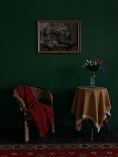 two chairs and a table with a vase on it in front of a green wall