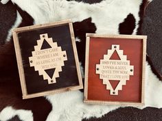 two wooden plaques with native sayings on them sitting on a cowhide rug, one is black and the other is brown