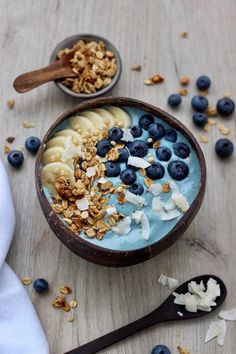 a bowl filled with granola and blueberries next to spoons on a table