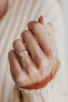 a woman's hand with a gold ring on her left wrist, wearing a white sweater