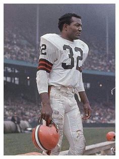 a football player standing on the sidelines with an orange jug in his hand and people watching from the bleachers