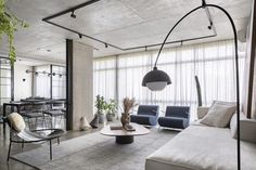 a living room filled with furniture next to a tall glass window covered in curtains and plants