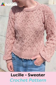 a woman wearing a pink sweater and jeans with her hands in her pockets while standing next to a wall