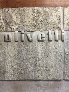 the word olivetti written in metal letters on a stone wall