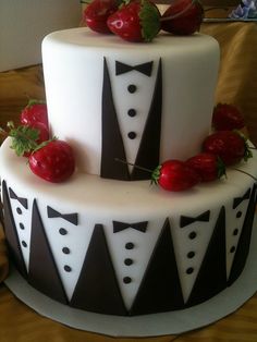 a white and black cake with red strawberries on the top, sitting on a table