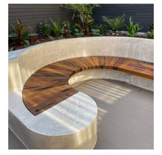 a curved wooden bench sitting on top of a cement wall next to a planter