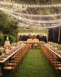 an outdoor wedding reception setup with string lights and wooden chairs, greenery and flowers on the tables