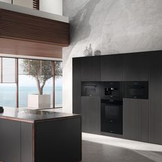 a modern kitchen with black cabinets and marble counter tops, along with a large window overlooking the ocean