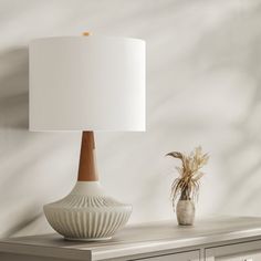 a white lamp sitting on top of a table next to a vase with a plant