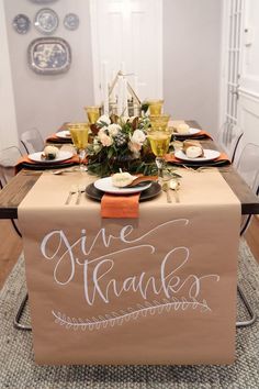 a table set for thanksgiving dinner with place settings and napkins on it, along with an orange ribbon that says give thanks