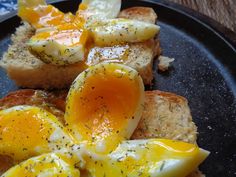 eggs and toast on a black plate with seasoning sprinkled around them, sitting on a wooden table