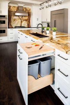 a kitchen with white cabinets and an island in the middle that has two trash cans on it