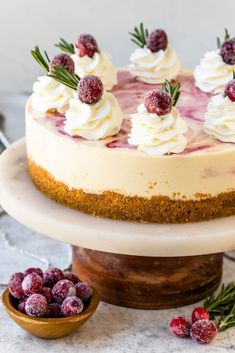 a cheesecake topped with whipped cream and fresh berries on a cake stand next to some cranberries