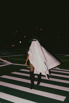 a woman walking across a cross walk wearing a long white coat and black knee high boots