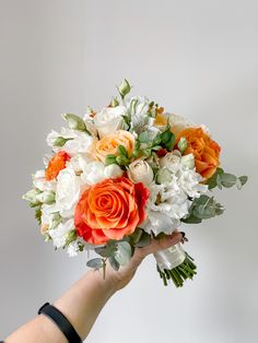 a person holding a bouquet of white and orange flowers with greenery in their hand