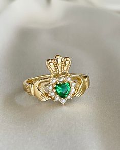 a gold ring with green and white stones on the front, sitting on a white cloth