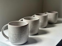 four coffee mugs lined up on top of a white counter with no one in them