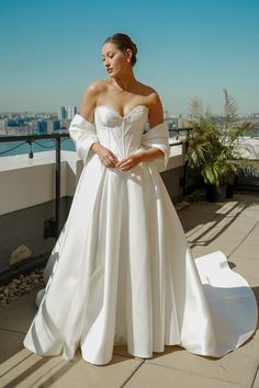 a woman in a white wedding dress standing on a balcony with the city behind her