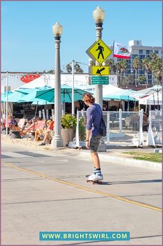 a man riding a skateboard down a street next to a tall pole with a pedestrian sign on it