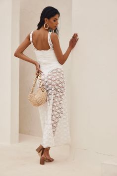 a woman standing in front of a white wall holding a straw bag and looking at the camera