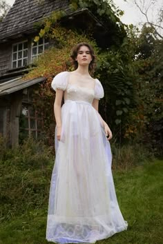 a woman wearing a white dress standing in front of a house