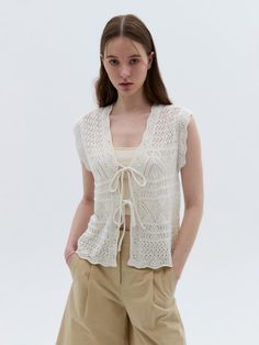 a woman standing in front of a white background wearing beige pants and a crochet top