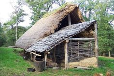 an old thatched roof house with wood and grass on the roof, surrounded by trees