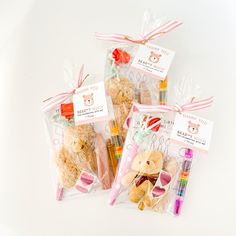 three packaged teddy bears are sitting next to each other in cellophane bags with writing utensils on them