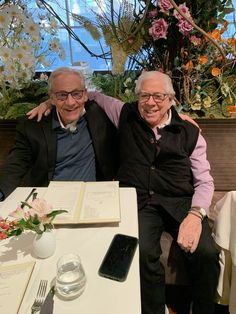 two men sitting next to each other at a table with flowers and books on it