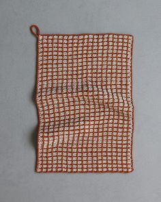 an orange and white checkered cloth hanging from a hook on a gray wall with a brown cord