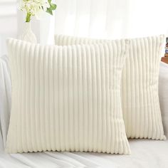 two white pillows sitting on top of a bed next to a vase filled with flowers