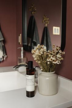 a white vase filled with flowers sitting on top of a bathroom counter next to a mirror