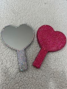 a heart shaped mirror sitting on top of a bed next to a pink hand mirror